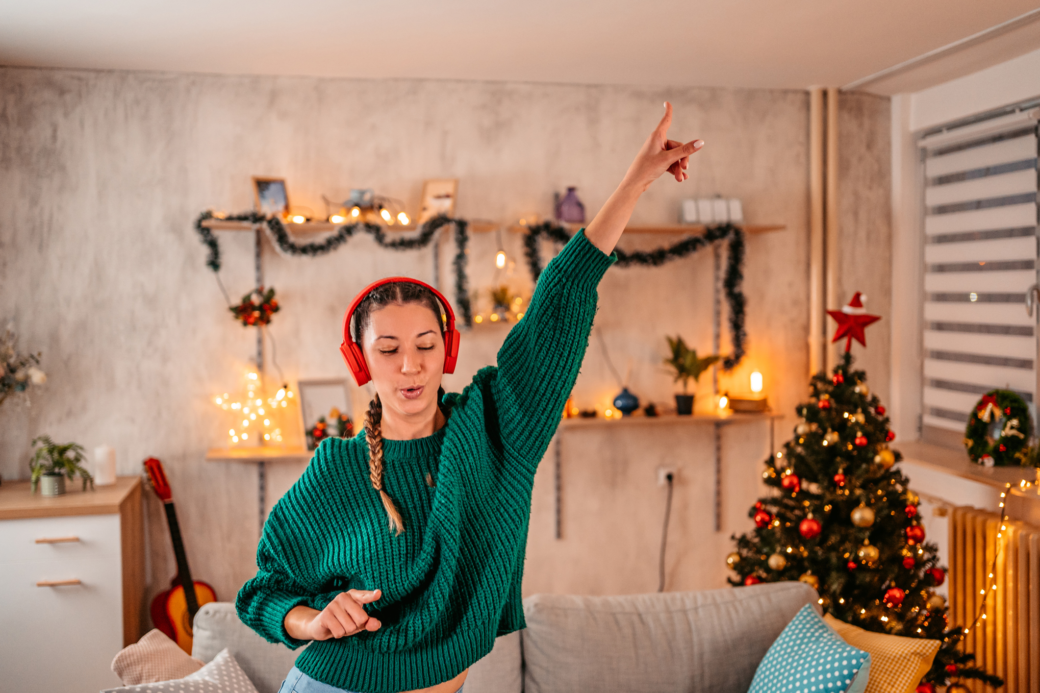 Beautiful young woman listening music on headset, singing and dancing at home at Christmas time.