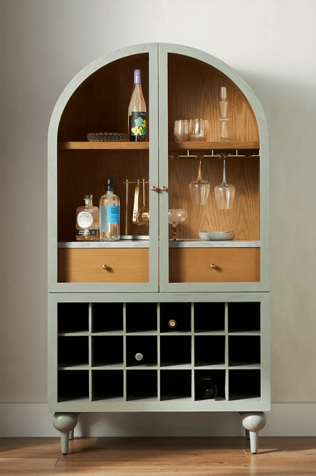 A large sage green bar cabinet filled with barware and glassware