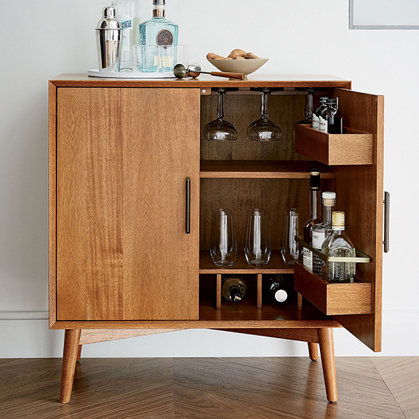 A half-open midcentury modern bar cabinet that's lined with glassware and topped with barware
