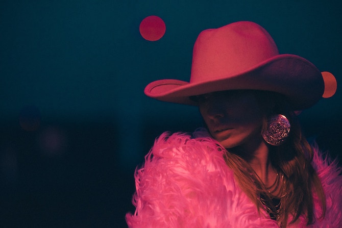 A person wearing a pink cowboy hat and a pink feather top