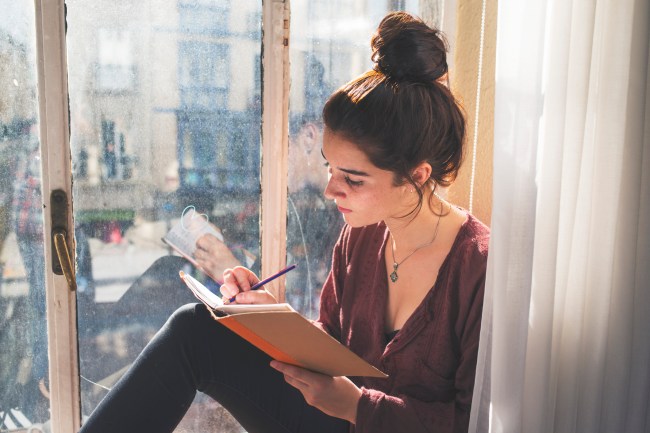 Young woman writes next to the window.