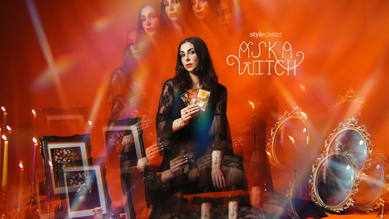 Roya holding tarot cards, surrounded by lit candles, small mirrors, and framed photos