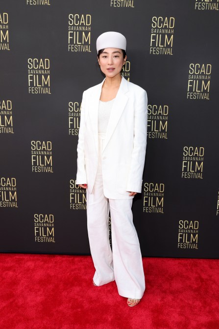 Greta Lee in a white three-piece suit and matching white hat at the SCAD Savannah Film Festival red carpet