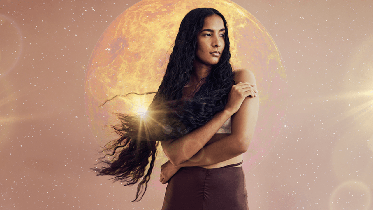 A woman with a mane of long flowing dark brown hair standing in front of planet Venus with sunlight peaking in from behind her