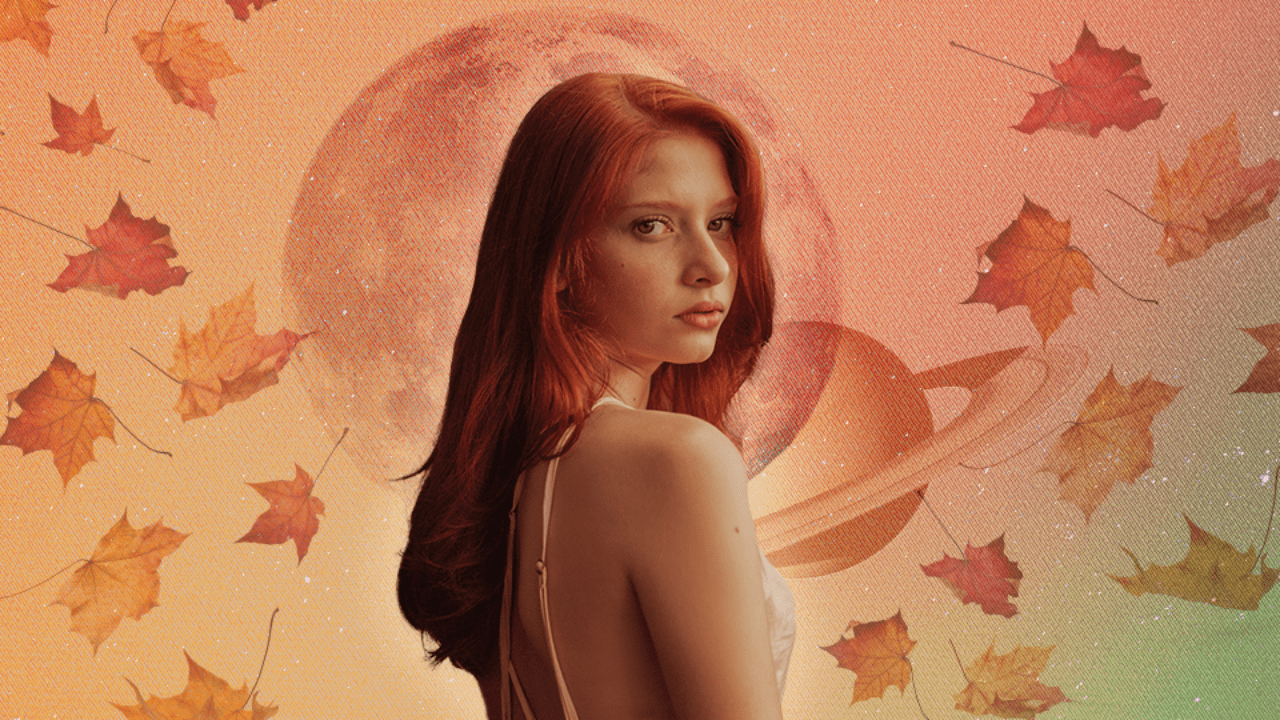 A woman with red hair standing in front of a full moon and planet Saturn with fall leaves floating around her