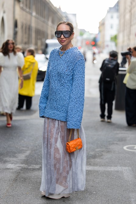 Sonia Lyson wears blue oversized jumper, orange bag, transparent white skirt, necklace, sunglasses outside Rotate during day four of the Copenhagen Fashion Week (CPHFW) SS25 on August 08, 2024 in Copenhagen, Denmark.