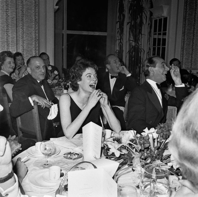 Actress Maggie Smith laughs while seated at a dining table during the Evening Standard Drama Awards for 1957, February 11th 1958. Seated next to her is musical conductor Sir Malcolm Sargent (1895-1967), and behind left, producer Sir Michael Balcon (1896-1977) and actor Nigel Patrick (1912-1981), behind right.