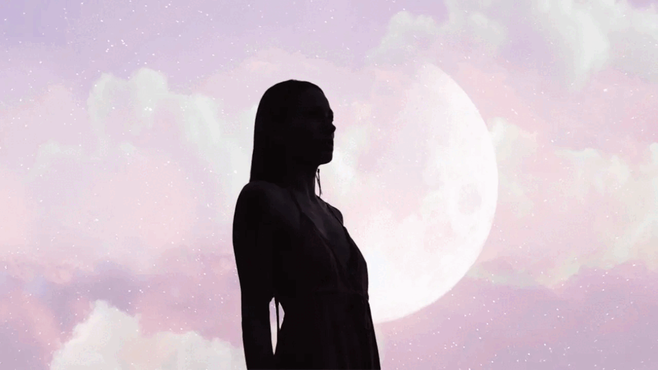 A dark silhouette of a woman in front of a full moon and white clouds drifting over a pink sky