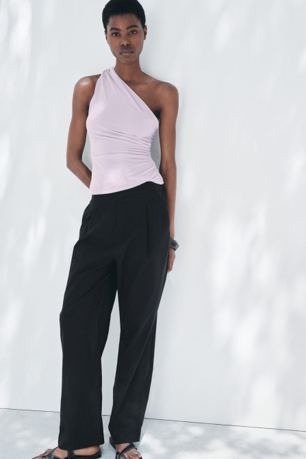 A model wearing the Zara Ruched Asymmetric Top in lilac paired with black trousers